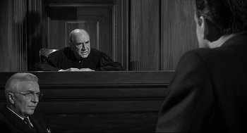 Movie still from “Anatomy of a Murder” (1959), directed by Otto Preminger – An older man in a courtroom looking at his reflection in a mirror; Medium shot, Low angle