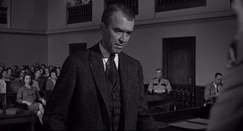 Movie still from “Anatomy of a Murder” (1959), directed by Otto Preminger – A man wearing a suit and tie in a courtroom; Medium shot, Over the shoulder angle