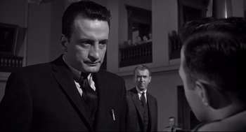Movie still from “Anatomy of a Murder” (1959), directed by Otto Preminger – A man in a suit and tie standing next to another man in a suit and tie; Close Up shot, Over the shoulder angle