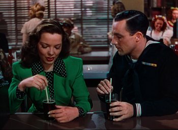 Movie still from “Anchors Aweigh” (1945), directed by Joseph Barbera – A man and a woman sitting at a table with drinks in front of them; Medium shot, High angle