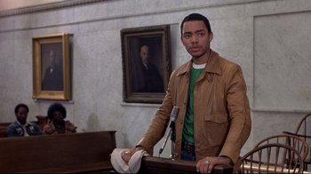 Movie still from “And Justice for All” (1979), directed by Norman Jewison – A man standing in front of a microphone in front of a painting; Medium shot, Over the shoulder angle