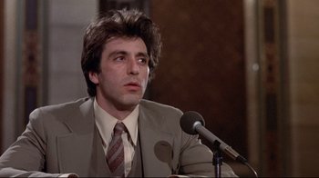 Movie still from “And Justice for All” (1979), directed by Norman Jewison – A man in a suit and tie sitting in front of a microphone; Close Up shot, Low angle