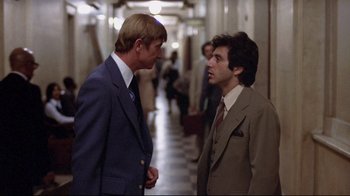 Movie still from “And Justice for All” (1979), directed by Norman Jewison – Two men in business suits talking to each other in an office hallway; Medium shot, Over the shoulder angle