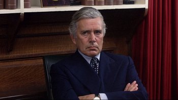 Movie still from “And Justice for All” (1979), directed by Norman Jewison – An older man wearing a suit and tie with his arms crossed sitting in a chair; Close Up shot, Over the shoulder angle