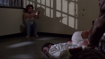 Movie still from “And Justice for All” (1979), directed by Norman Jewison – A man sitting on the ground in a room while another man is sitting on the floor and holding a cell phone in his hand; Wide shot, High angle