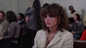 Movie still from “And Justice for All” (1979), directed by Norman Jewison – A woman in a white jacket is sitting in front of a group of people; Close Up shot, Over the shoulder angle