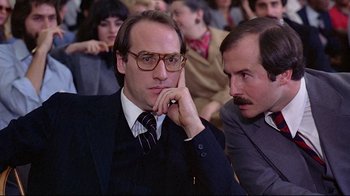 Movie still from “And Justice for All” (1979), directed by Norman Jewison – A man in a suit sitting next to another man in a tie; Close Up shot, Over the shoulder angle