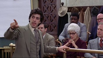 Movie still from “And Justice for All” (1979), directed by Norman Jewison – A group of people in a room with a man in a suit; Medium shot, Over the shoulder angle