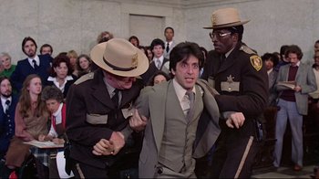 Movie still from “And Justice for All” (1979), directed by Norman Jewison – A group of people in a room with a man in a suit; Medium shot, Low angle