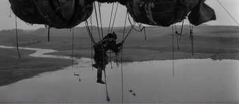 Movie still from “Andrei Rublev” (1966), directed by Andrei Tarkovsky – A man hanging on to a rope while standing on a platform; Wide shot, Low angle