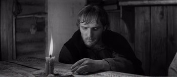 Movie still from “Andrei Rublev” (1966), directed by Andrei Tarkovsky – A man sitting at a table with a lit candle in front of him; Close Up shot, High angle