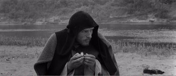 Movie still from “Andrei Rublev” (1966), directed by Andrei Tarkovsky – A man in a hooded cloak holding a piece of food; Close Up shot, High angle