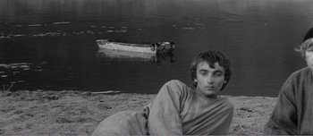 Movie still from “Andrei Rublev” (1966), directed by Andrei Tarkovsky – A man sitting on the shore of a body of water; Medium shot, High angle