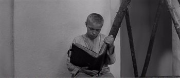 Movie still from “Andrei Rublev” (1966), directed by Andrei Tarkovsky – A young boy holding an open book in front of a white wall; Medium shot, High angle