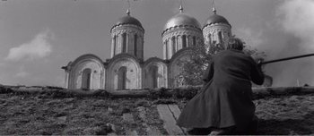 Movie still from “Andrei Rublev” (1966), directed by Andrei Tarkovsky – A black - and - white photo of a person standing in front of a building; Wide shot, Low angle