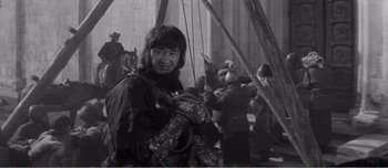 Movie still from “Andrei Rublev” (1966), directed by Andrei Tarkovsky – A man holding a baby in his arms while standing in front of a group of people; Medium shot, High angle