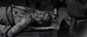Movie still from “Andrei Rublev” (1966), directed by Andrei Tarkovsky – A man is laying on a wooden table with his hands on his head; Medium shot, High angle