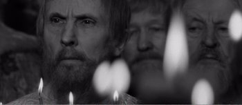 Movie still from “Andrei Rublev” (1966), directed by Andrei Tarkovsky – Two men are standing next to candles in a black and white photo; Close Up shot, Over the shoulder angle