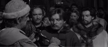 Movie still from “Andrei Rublev” (1966), directed by Andrei Tarkovsky – A group of men standing around each other holding a knife; Medium shot, Over the shoulder angle