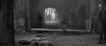 Movie still from “Andrei Rublev” (1966), directed by Andrei Tarkovsky – A black and white photo of people sitting in an archway; Wide shot, High angle