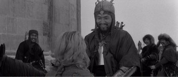 A man wearing a crown and holding a sword talking to a woman