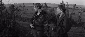 Movie still from “Andrei Rublev” (1966), directed by Andrei Tarkovsky – Two people in a field with trees in the background; Medium shot, Over the shoulder angle