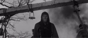 Movie still from “Andrei Rublev” (1966), directed by Andrei Tarkovsky – A black and white photo of a man in a hood; Medium shot, Low angle