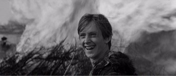 Movie still from “Andrei Rublev” (1966), directed by Andrei Tarkovsky – A young man smiling for the camera in front of trees; Close Up shot, Over the shoulder angle