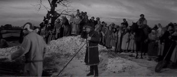 Movie still from “Andrei Rublev” (1966), directed by Andrei Tarkovsky – An old photo of a man holding a stick in front of a crowd; Wide shot, High angle