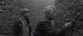 Movie still from “Andrei Rublev” (1966), directed by Andrei Tarkovsky – A man and a woman standing next to each other in front of a stone wall; Medium shot, Over the shoulder angle