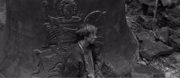 Movie still from “Andrei Rublev” (1966), directed by Andrei Tarkovsky – A man sitting in front of a statue of a horse; Medium shot, Overhead angle