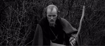 Movie still from “Andrei Rublev” (1966), directed by Andrei Tarkovsky – An old man with a beard is sitting in front of a tree; Medium shot, High angle