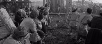 Movie still from “Andrei Rublev” (1966), directed by Andrei Tarkovsky – A black and white photo of a group of people standing in the mud; Wide shot, High angle