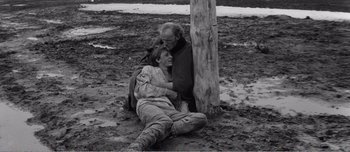 Movie still from “Andrei Rublev” (1966), directed by Andrei Tarkovsky – A man and a woman sitting next to a tree in the mud; Medium shot, High angle