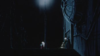Movie still from “Angel's Egg” (1985), directed by Mamoru Oshii – Two people sitting on steps in front of a building at night; Wide shot, Low angle