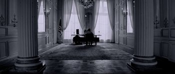 Movie still from “Angel-A” (2005), directed by Luc Besson – A man sitting at a desk in a room with curtains; Wide shot, High angle