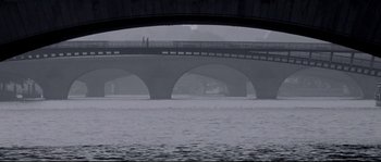Movie still from “Angel-A” (2005), directed by Luc Besson – Two people walking on a bridge over a body of water; Extreme Wide shot, High angle