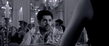 Movie still from “Angel-A” (2005), directed by Luc Besson – A black and white photo of a man sitting at a dinner table; Close Up shot, Over the shoulder angle