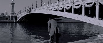 Movie still from “Angel-A” (2005), directed by Luc Besson – A man standing in the middle of a body of water near a bridge; Wide shot, Low angle