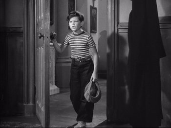 Movie still from “Angels with Dirty Faces” (1938), directed by Michael Curtiz – A young boy is standing in a doorway holding a hat; Medium shot, High angle