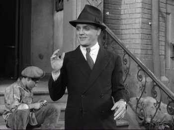 Movie still from “Angels with Dirty Faces” (1938), directed by Michael Curtiz – A man in a suit and hat standing next to a staircase; Medium shot, Low angle