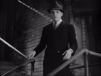 Movie still from “Angels with Dirty Faces” (1938), directed by Michael Curtiz – A black and white photo of a man wearing a suit and hat; Medium shot, Low angle