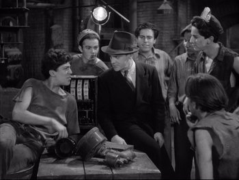 Movie still from “Angels with Dirty Faces” (1938), directed by Michael Curtiz – A group of people standing around a table; Medium shot, High angle