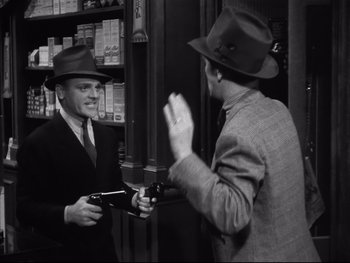 Movie still from “Angels with Dirty Faces” (1938), directed by Michael Curtiz – Two men in suits and hats talking to each other in a store; Medium shot, Over the shoulder angle