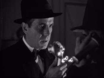 Movie still from “Angels with Dirty Faces” (1938), directed by Michael Curtiz – A black and white photo of a man in a hat holding a flashlight; Close Up shot, Low angle