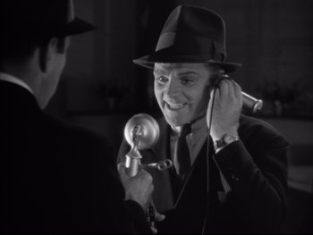 Movie still from “Angels with Dirty Faces” (1938), directed by Michael Curtiz – A man in a suit and a hat is holding a microphone; Close Up shot, Low angle
