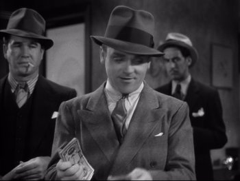 Movie still from “Angels with Dirty Faces” (1938), directed by Michael Curtiz – A black and white photo of a man in a suit and hat; Medium shot, Low angle