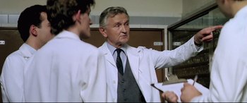 Movie still from “Anguish” (1987), directed by Bigas Luna – A man in white lab coat talking to another man; Medium shot, Low angle