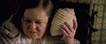 Movie still from “Anguish” (1987), directed by Bigas Luna – An older woman holding a shell in front of her face; Close Up shot, High angle