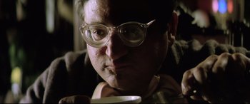 Movie still from “Anguish” (1987), directed by Bigas Luna – A person wearing glasses and holding a cup; Close Up shot, Low angle